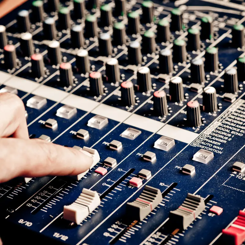 A mixing desk. A finger is on one of the sliders moving it up or down.